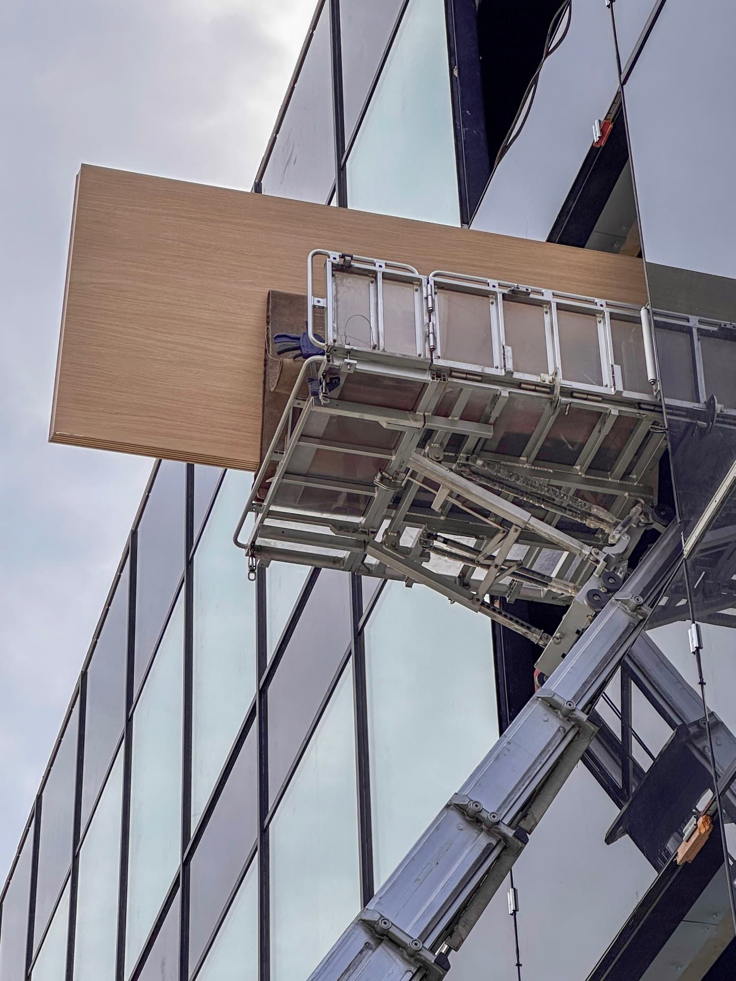 Plateau van de ladderlift met een vastgezette plaat, hoog tegen een glasgevel