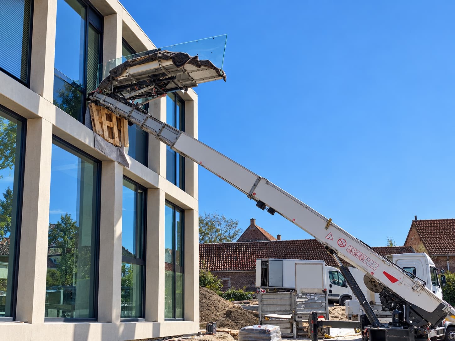 Ladderlift brengt een glaspaneel op het plateau naar de bovenverdieping van een nieuwbouw met glasgevel